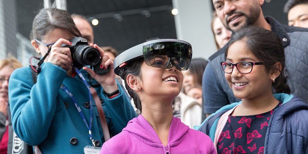A smiling girl wearing Virtual Reality Headsets at the Great Exhibition Road Festival 2019 surrounded by spectators.