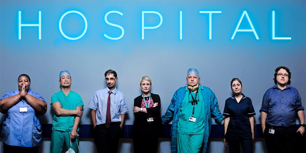 Doctors and nurses posing in front of a neon blue sign reading 'HOSPITAL'.