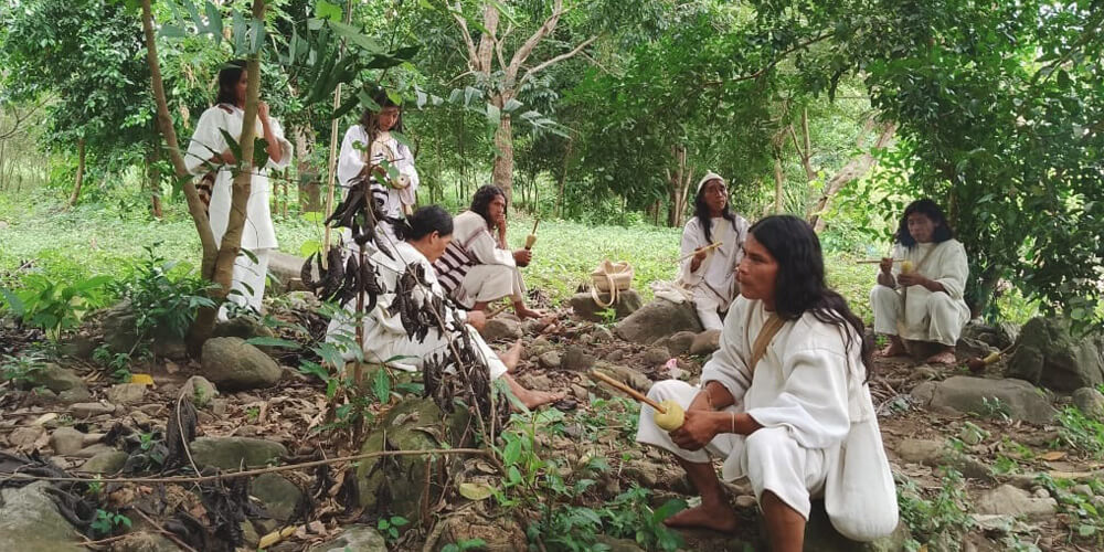 Seven members of the indigenous South American Kogi community sitting and standing in the forest of the Sierra Nevada de Santa Marta mountain range in Colombia.