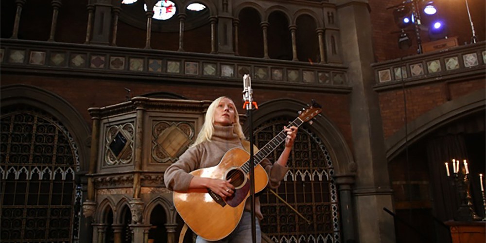 Singer Songwriter, Laura Marling, with long, straight blond hair, strumming guitar at Union Chapel main auditorium