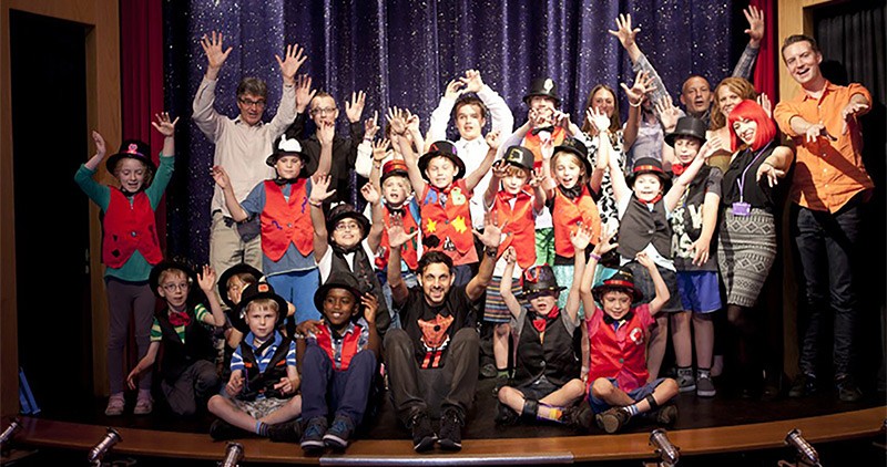 A large group of children with magicians, including Dynamo, on stage