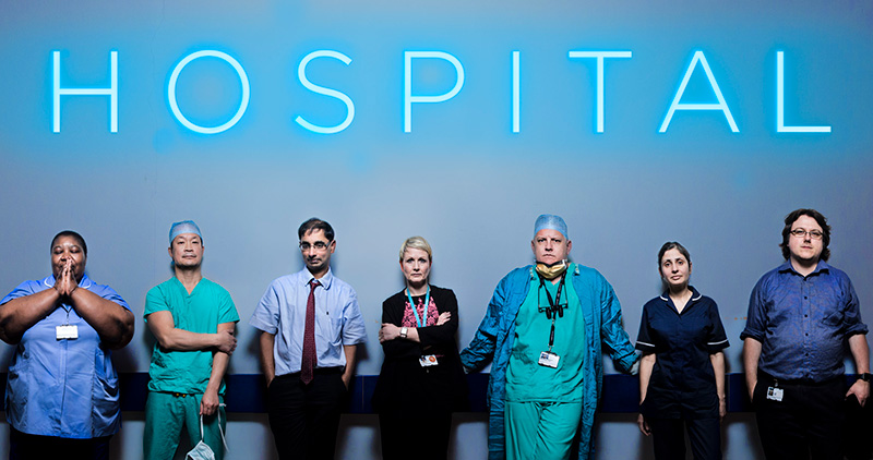 Doctors and nurses posing in front of a neon blue sign reading 'HOSPITAL'.