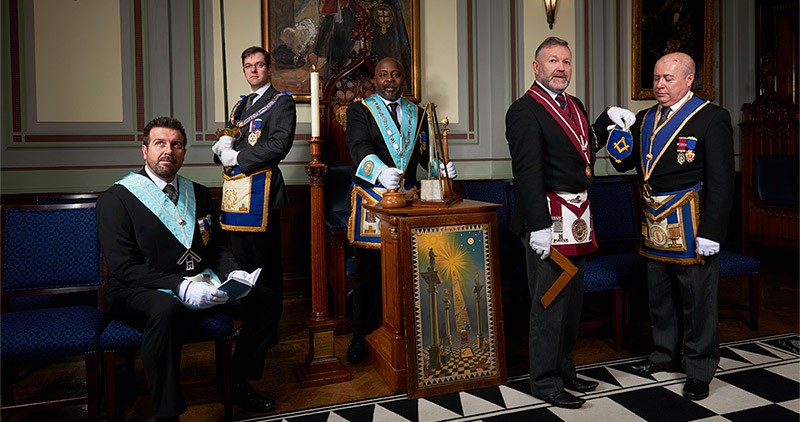 Five freemasons dressed in full regalia and holding Masonic artefacts
