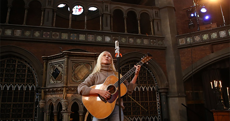Singer Songwriter, Laura Marling, with long, straight blond hair, strumming guitar at Union Chapel main auditorium